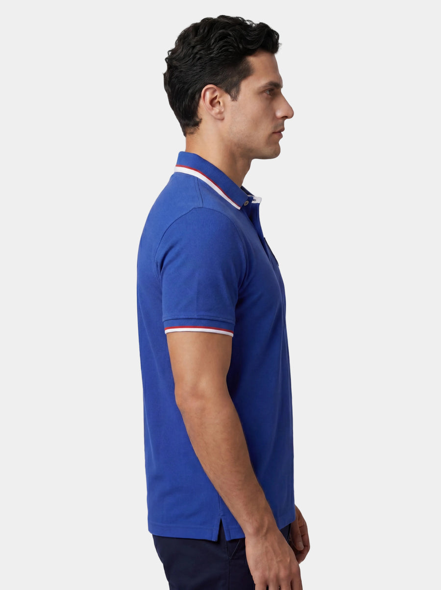 Man wearing a blue polo shirt with white trim on a light gray background.