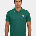 Man wearing a green polo shirt with a logo on a white background
