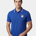 Man wearing a blue polo shirt with a USA logo on a light gray background